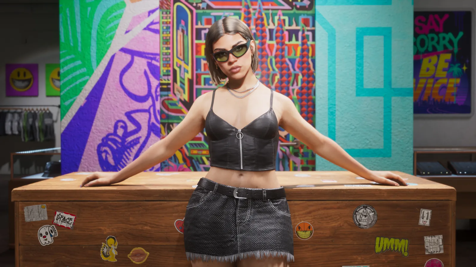 A woman in cat-eye sunglasses, a black leather bustier and a denim mini skirt leaning back on a sticker-covered wooden counter, bright murals and racks of clothing behind her.