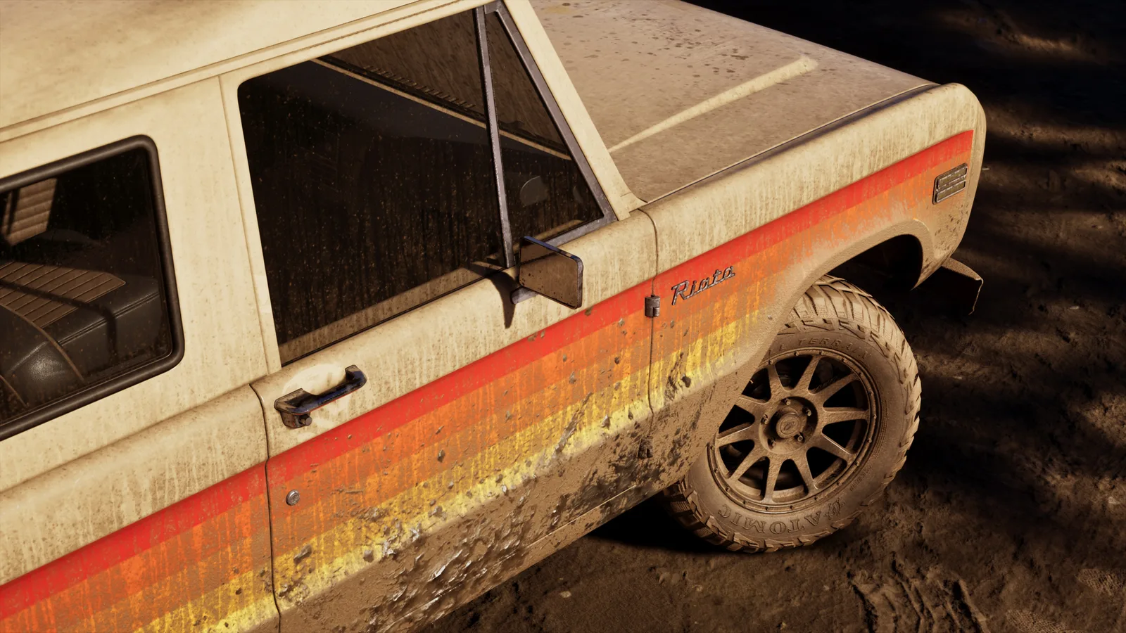 Close-up of a mud-splashed cream off-roader's flank carrying a red, orange and yellow stripe and a Riata script badge above a muddy all-terrain tyre.