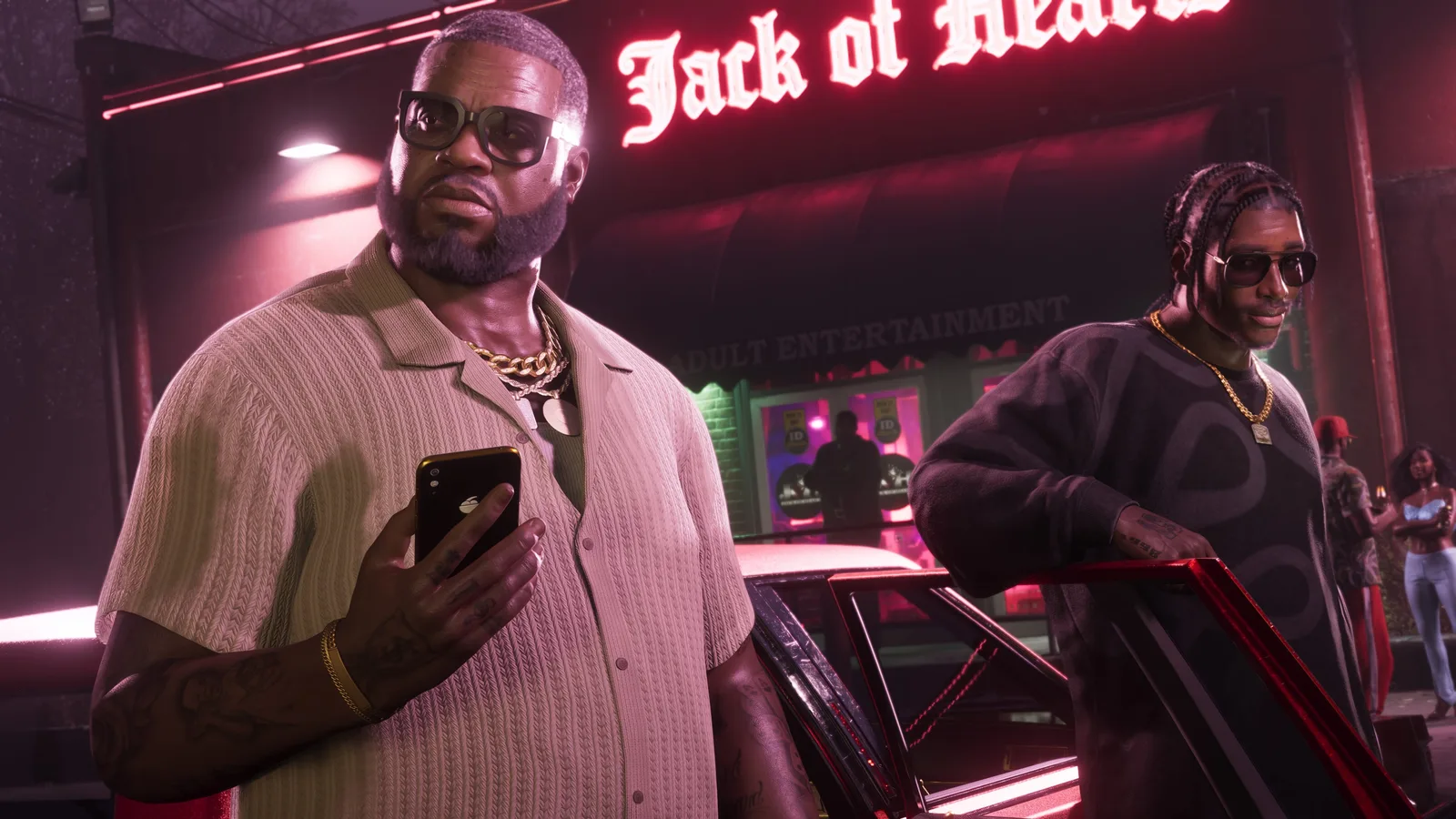 Boobie Ike in dark glasses, a cream knit shirt and gold chains holding a phone outside a neon-lit club at night, a younger man in braids standing at an open car door behind him.