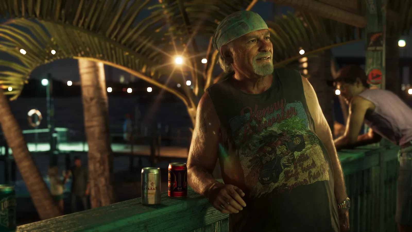 Brian Heder in a bandana and a graphic tank top leaning on a green wooden rail at a waterfront bar at night, two beer cans on the rail beside him and string lights over the water behind.
