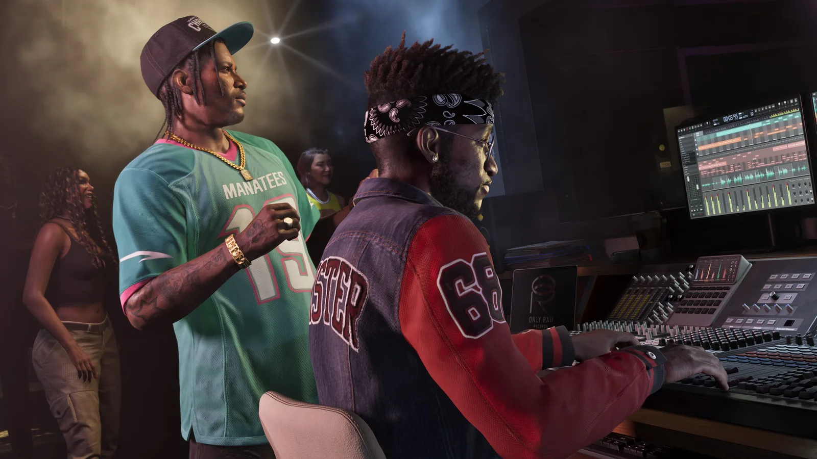 DreQuan Priest in a green sports jersey and gold chain standing behind a seated engineer at a large mixing desk in a recording studio, editing software on the screen above.