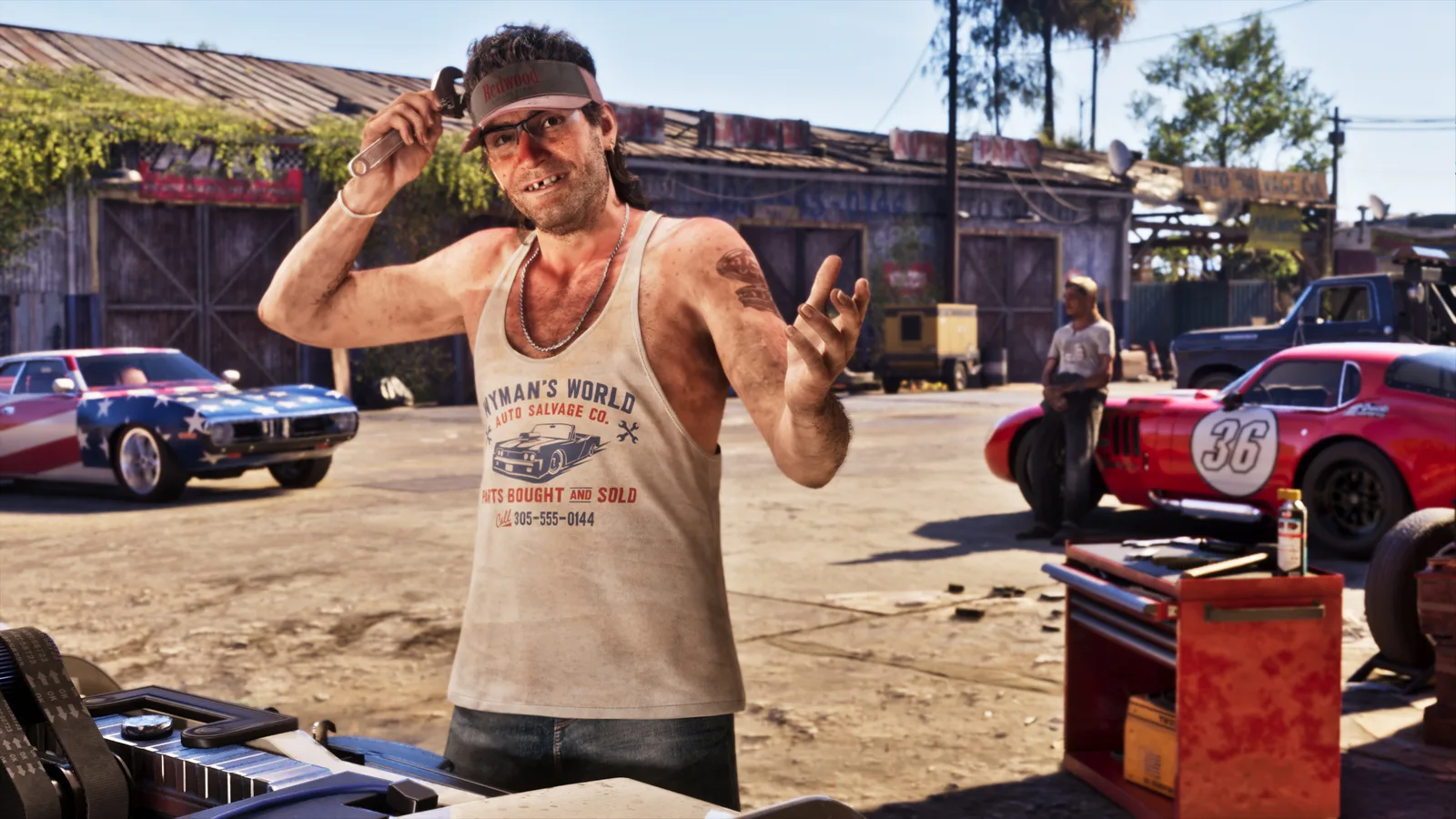 A grinning man in a Redwood visor and a Wyman's World Auto Salvage Co. tank top raising an adjustable wrench in his right hand beside his head, a stars-and-stripes muscle car and a red number 36 racer parked either side of him and open timber workshop bays and an auto salvage sign behind, in a sunlit yard.
