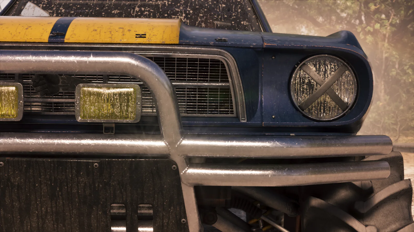 Close-up of the mud-splashed blue and yellow buggy's front end — a tubular bull bar, a round headlight taped over with an X, yellow fog lamps and a mesh grille.
